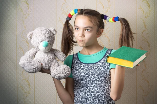 Menina de 11 anos segurando um livro em uma mão e um urso de pelúcia na outra — Fotografia de Stock