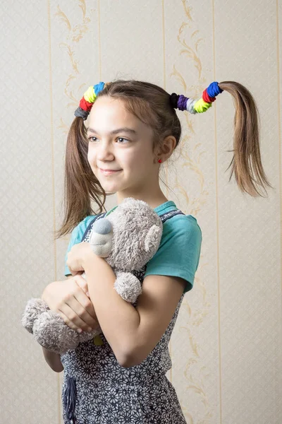 Retrato de menina de 11 anos com caudas engraçadas de elásticos abraçando ursinho de pelúcia — Fotografia de Stock