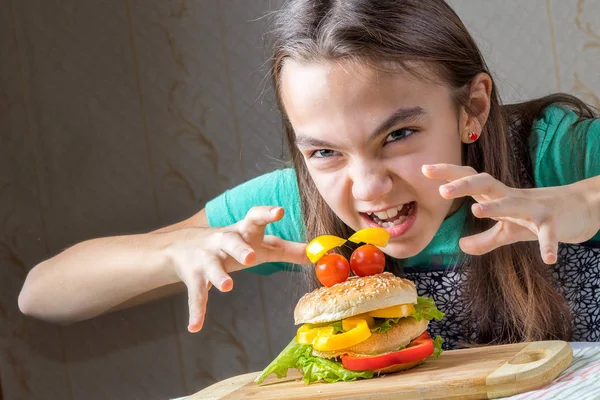 Lány türelmetlenül lecsapott egy hamburger, kinyújtotta a karját, neki egy görbe ujjaival — Stock Fotó