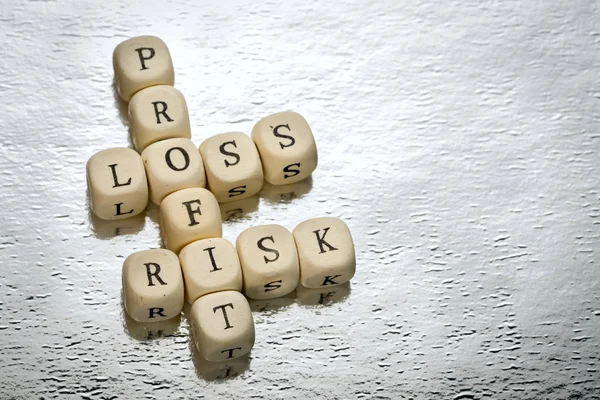 profit loss risk crossword on a wooden cubes on a shiny silver background