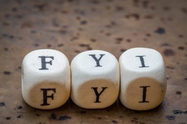 FYI (For Your Information) text on wooden cubes on a brown cork background