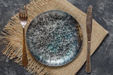 siyah çimento zemin üzerine koyu eski el yapımı dökme demir plaka çatal bıçak takımı ile Üstten Görünüm.