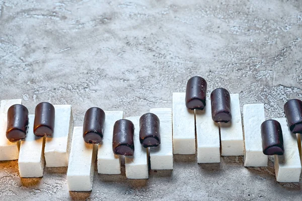 Teclas de piano dispostas chocolates doces e pasta marshmallows, em um fundo de cimento bege neutro com muito espaço de cópia acima. Conceito de música doce . — Fotografia de Stock