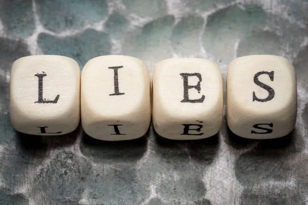 The word lies, lined with wooden blocks on a metal forged textural background. — Stock Photo, Image