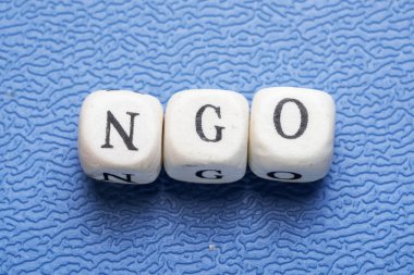 Word NGO (non governmental organization) on a wooden cubes on a blue background clipart