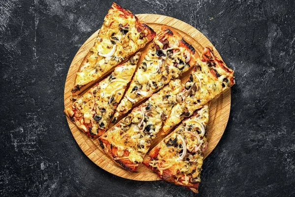 beautifully laid herringbone pieces of pizza on a circular wooden board on a dark black textural background.
