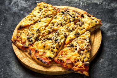 güzel bir dairesel ahşap tahta koyu siyah dokusal zemin, yan görünüm üzerinde balıksırtı dilim pizza koydu.