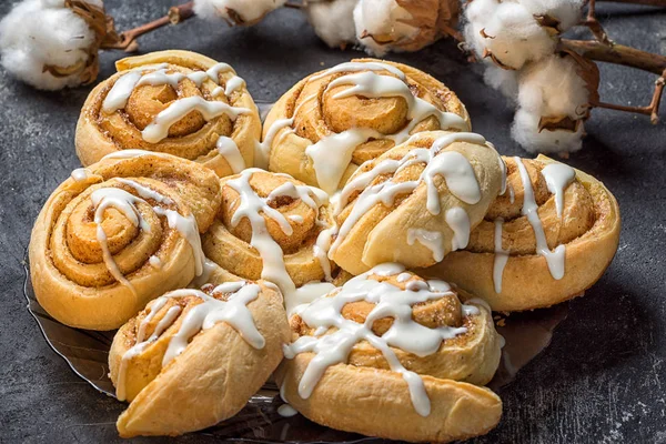 French sweet cinnamon rolls on a plate on a dark background, with cotton bolls in the background — Stock Photo, Image