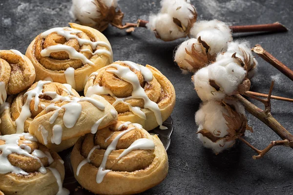 Fresh cinnamon rolls close up side view, dark grey cement background, cotton boxes behind — Stock Photo, Image