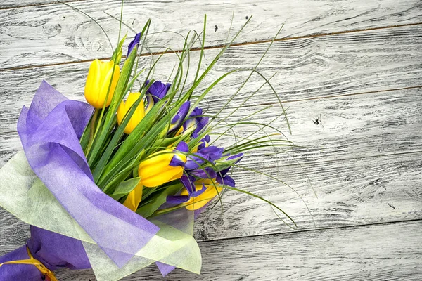 Ramo de tulipanes amarillos y lirios azules se encuentra casualmente en una mesa de madera con un espacio de copia . —  Fotos de Stock