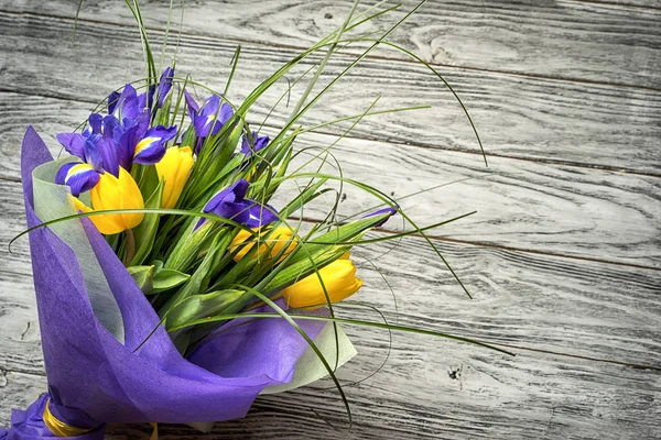 Ramo de tulipanes amarillos y lirios azules se encuentra casualmente en una mesa de madera con un espacio de copia . —  Fotos de Stock