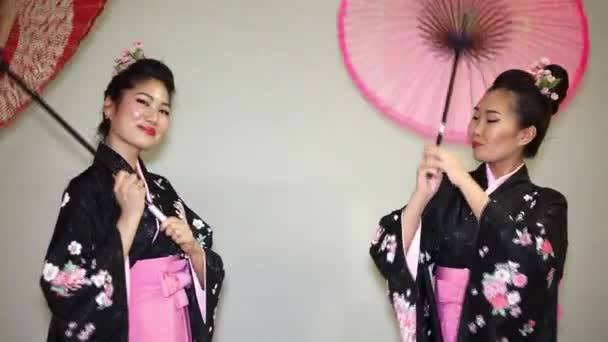 Twee prachtige geisha in een traditionele Japanse kimono glimlachend en draaien van parasols — Stockvideo