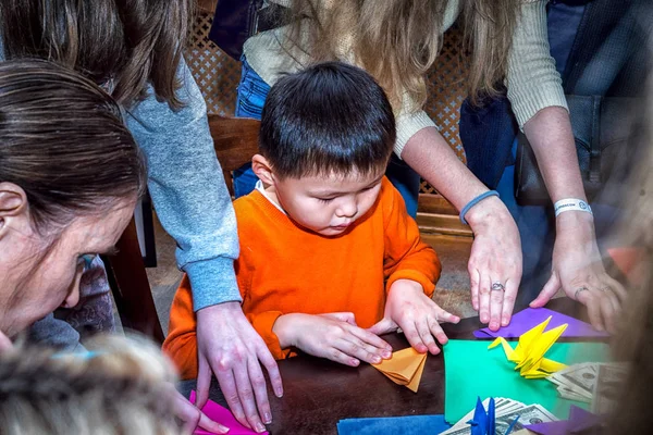 Moskwa, Rosja - 4 listopada 2016: Iv akcja ogólnomiejskich festiwalu "Night of the Arts". Chłopiec Dokonywanie origami żuraw w Dk Nagorniy. Wielu dorosłych wokół, aby pomóc mu. — Zdjęcie stockowe