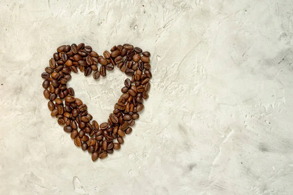 Silhueta pequena forma de coração feita de grãos de café torrados em um fundo de cimento neutro com espaço de cópia — Fotografia de Stock