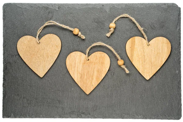 Tres corazones de madera sobre una placa rectangular de piedra negra aislada sobre fondo blanco — Foto de Stock