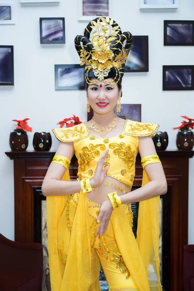 Красивая азиатская девушка в традиционном желтом китайском костюме сцены стоя у стены с картинками и камином — стоковое фото