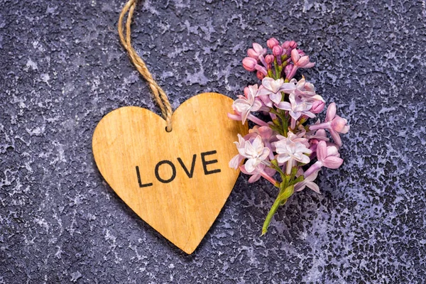 Un ramo de lilas y corazón de madera con la palabra amor en él sobre un fondo de cemento de textura azul — Foto de Stock