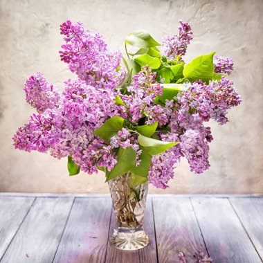 Leylak ahşap bir masa tarafsız bej renkli arka plan üzerinde şeffaf bir vazoda buket natürmort