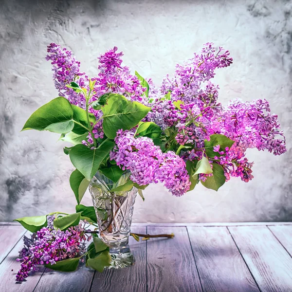 Stilleven boeket van lila in een kristallen vaas op de achtergrond van een getextureerde muur — Stockfoto