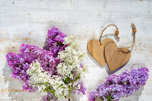 Dois corações de madeira com espaço de cópia para o seu texto e um monte de flores lilás no fundo pintado de madeira — Fotografia de Stock