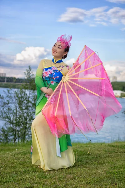 Vacker kinesisk flicka i traditionell kinesisk klänning med fläkt på åstranden — Stockfoto