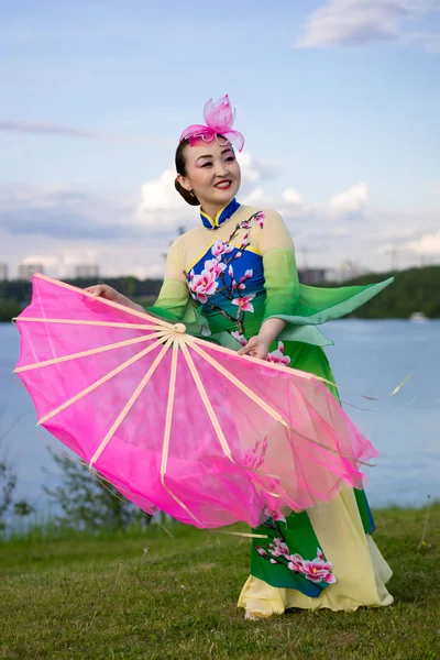 Vacker kinesisk flicka i traditionell kinesisk klänning med fläkt på åstranden — Stockfoto