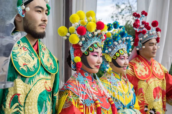 Group of four asian people men and women standing in a row and greeting outdoor in traditional chinese costumes, profile view — Stock Photo, Image