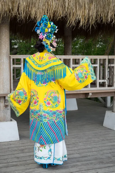 Красивая китайская девушка в традиционном китайском платье с длинными рукавами и шляпой с помпонами, стоящими позади на открытом воздухе и превращая руку в prifile — стоковое фото