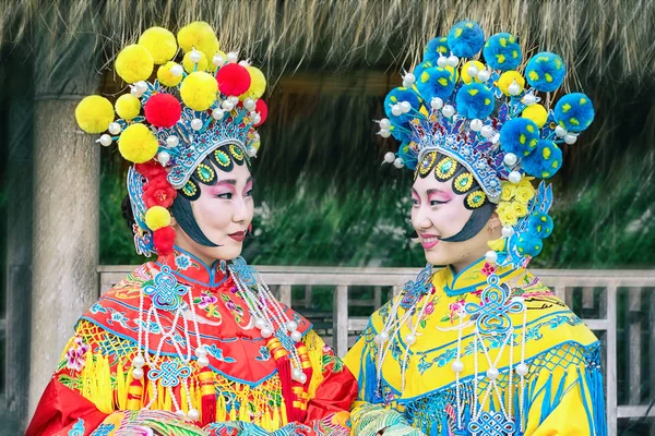Porträtt av två vackra kinesiska flickor i traditionell kinesisk klänning och hatt med pomponger tittar varandra — Stockfoto