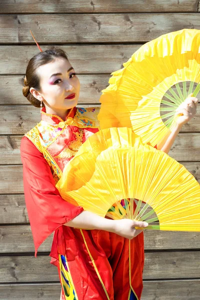 Portrait of beautiful chinese girl in traditional red chinese dress with two big yellow fans — Stock Photo, Image