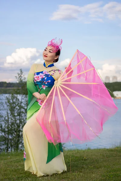 Vacker kinesisk flicka i traditionell kinesisk klänning med fläkt på åstranden — Stockfoto