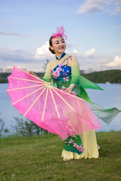 Vacker kinesisk flicka i traditionell kinesisk klänning med fläkt på åstranden — Stockfoto