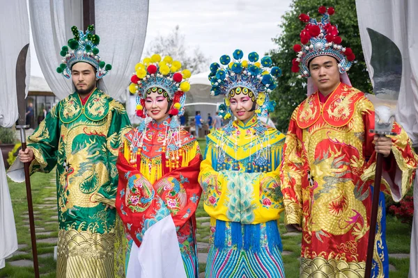 group of four asian people men and women standing in a row and greeting outdoor in traditional chinese costumes