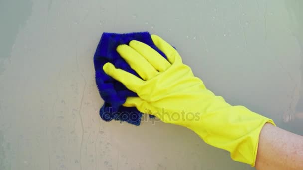 Женская рука в жёлтой перчатке с синей тряпкой для чистки матового стекла круговыми движениями, образующими круглую рамку — стоковое видео