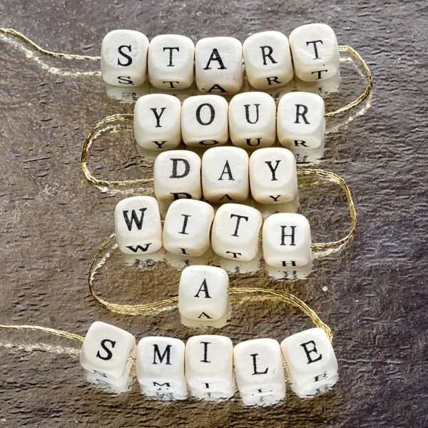 Inscription start your day with a smile made from wooden toy blocks stringed on a rope and laying on the shining foil background. — Stock Photo, Image