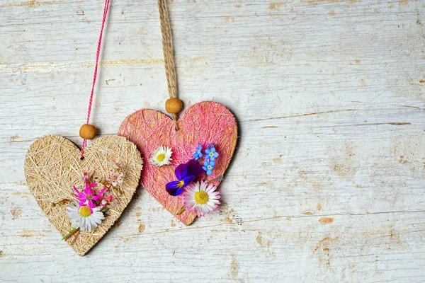 Dos corazones decorados con pequeñas flores silvestres cuelgan de una cuerda, y copiar el espacio en un viejo fondo pintado de madera para su texto — Foto de Stock