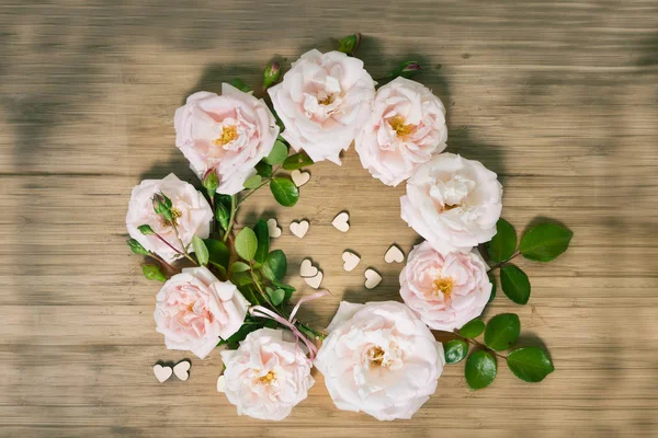 Розовые розы wrealh с маленькими деревянными сердцами на деревянном столе, вид сверху с копировальным пространством — стоковое фото