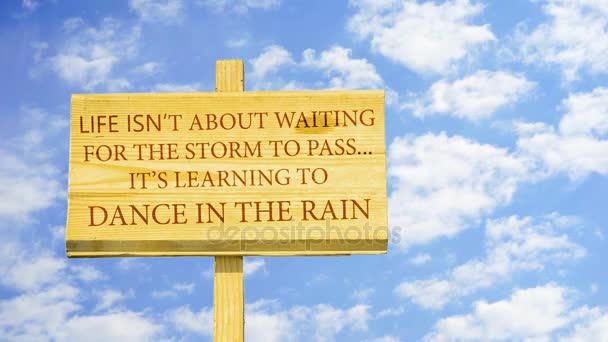 生活不是等待暴风雨过去。它学会跳舞在雨中，对时间流逝云在蓝蓝的天空中的一块木牌上的文字. — 图库视频影像