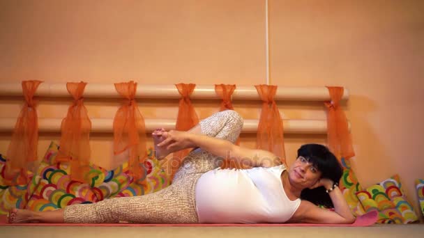 40 week pregnant middle aged caucasian woman laying on the side in asana doing yoga exercises and holding her leg up. — Stock Video