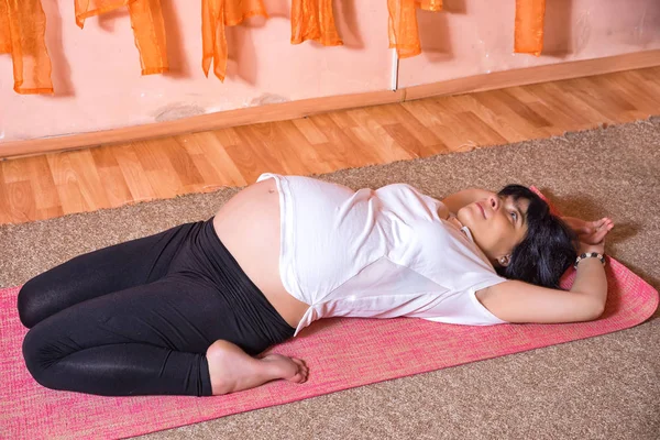 Pregnancy Yoga and Fitness concept. Healthy maternity lifestyle concept. 40 week pregnant middle aged caucasian woman doing yoga exercises laying leaning back.