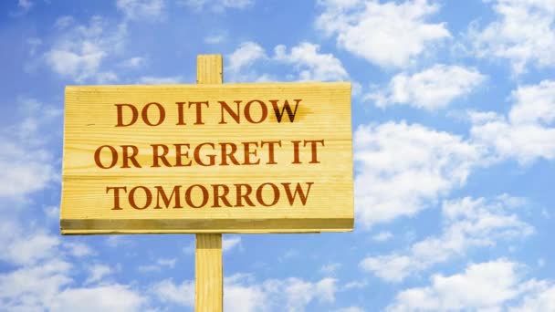 Fais-le maintenant ou regrette-le demain. Des mots sur un panneau en bois contre les nuages du temps dans le ciel bleu . — Video