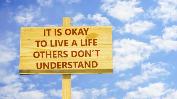 Es ist okay, ein Leben zu führen, das andere nicht verstehen. Worte auf einem Holzschild gegen Zeitraffer-Wolken am blauen Himmel. — Stockvideo