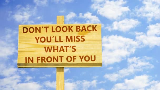 Don't look back. You will miss what is in front of you. Words on a wooden sign against time lapse clouds in the blue sky. — Stock Video
