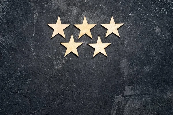 Five wooden stars arranged in two rows, 3 on the top and 2 below, on a dark cement background with copy of the space. Concept of service rating and quality of trade. Top view, copy space for your text — Stock Photo, Image