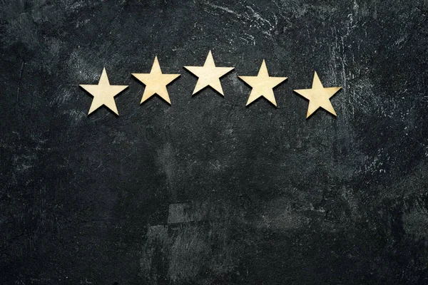 Five wooden stars located in the form of an arch or arc in the upper part of a dark cement background. Conceptual of service rating and quality of trade. Top view, copy space for your text. — Stock Photo, Image