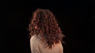 Genç güzel beyaz bir kadınla uzun kıvırcık saçlar geri dönüş ve saçları ile ön geliştirmek üzerinde siyah bir arka plan.