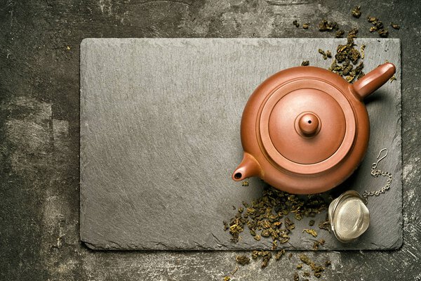 top view of a teapot made from red clay and brewing green Chinese tea with tea strainer, on a black stone tray and black grundy table with copy space for your text.