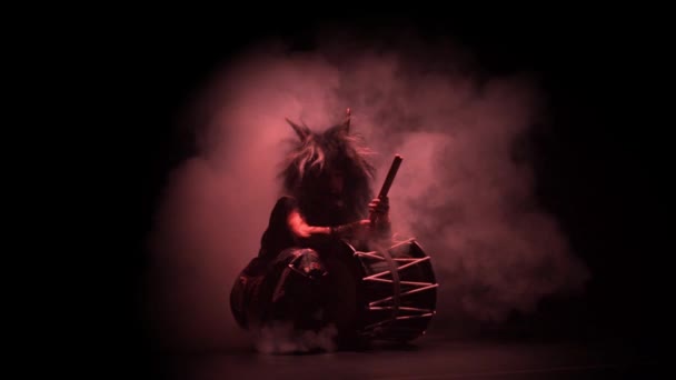 Taiko drummer in a wig and a demon mask on stage with drum on a black background and colorful smoke. Demon from Japanese mythology. — Stock Video