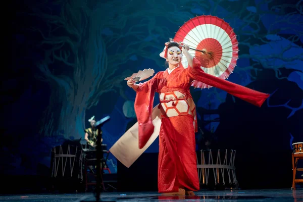 Traditional Japanese performance. Actress in red with umbrella and fan dancing turning.