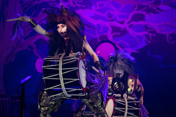 Taiko drummer in a wig and a demon mask performs on stage with drum on a dark background. Demon from Japanese mythology.